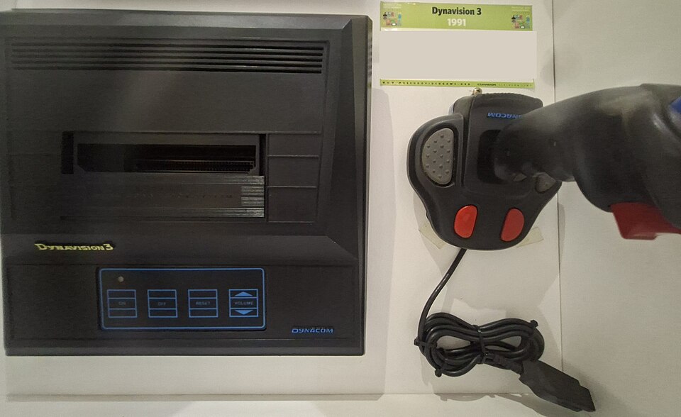 Dynavision 3 preto com painel de toque azul ao lado de um joystick Dynacom